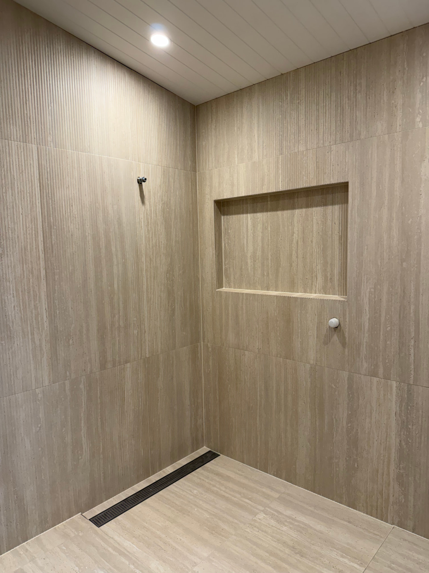Travertine-look tiled shower wall with a large recessed niche