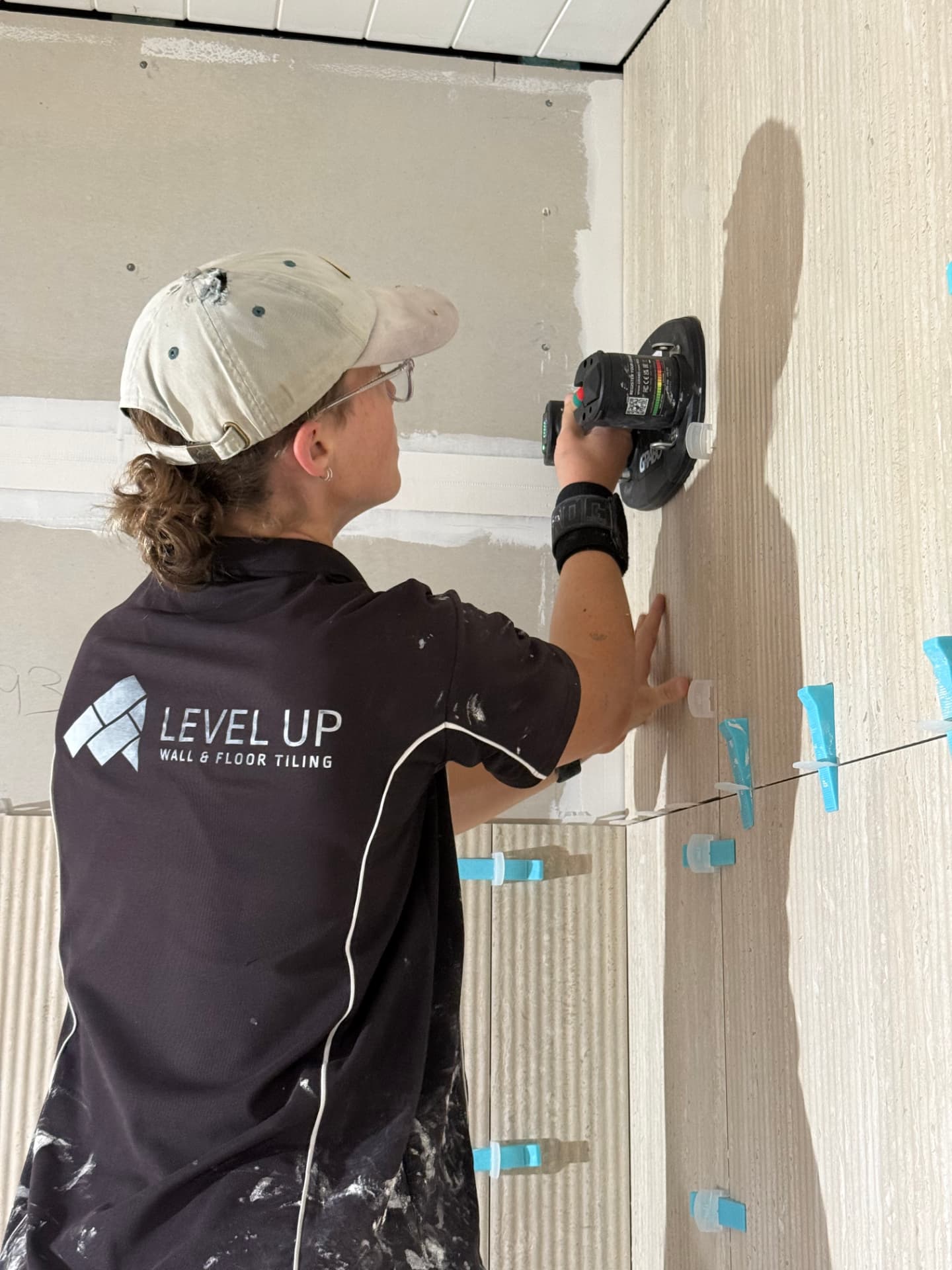 Sarah setting a wall tile in place wearing the Level Up Wall & Floor Tiling shirt