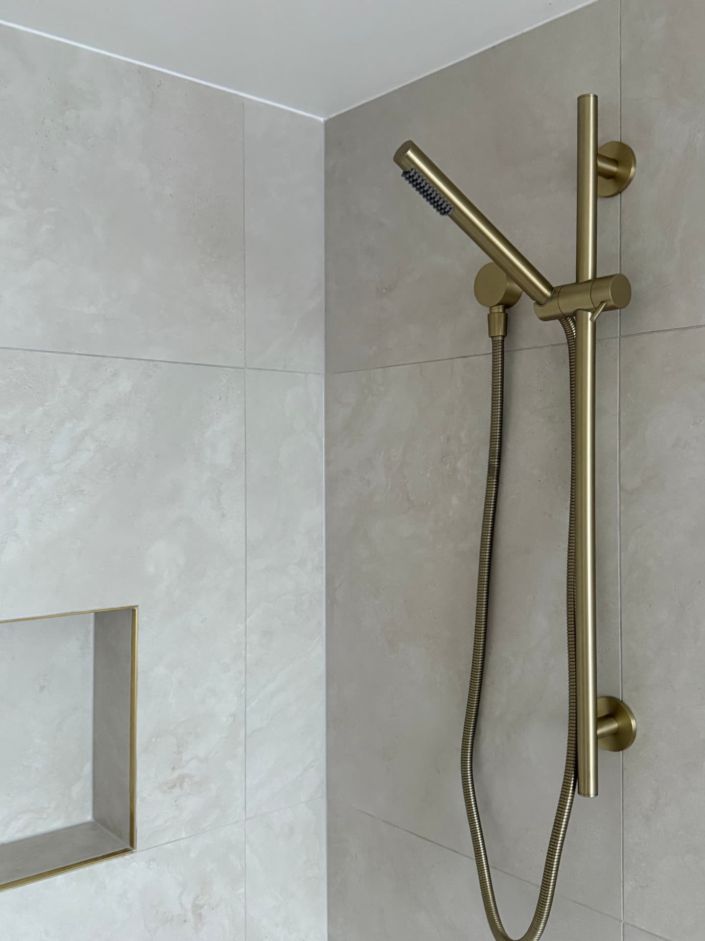 Brass hand shower beside a neatly tiled recessed niche