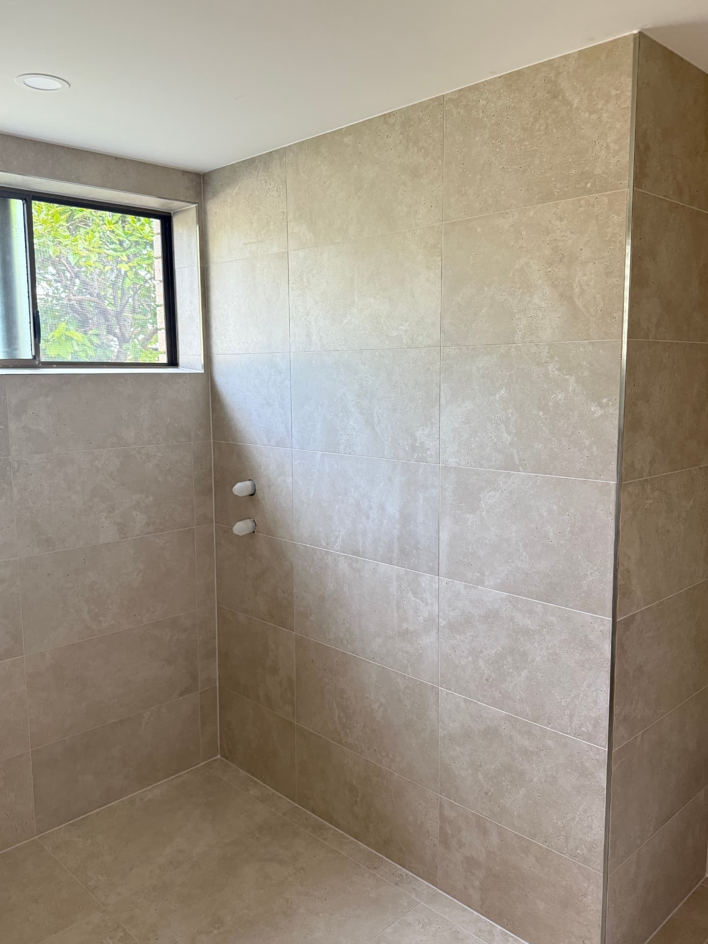 Stone-look tiled shower with a window looking out to greenery