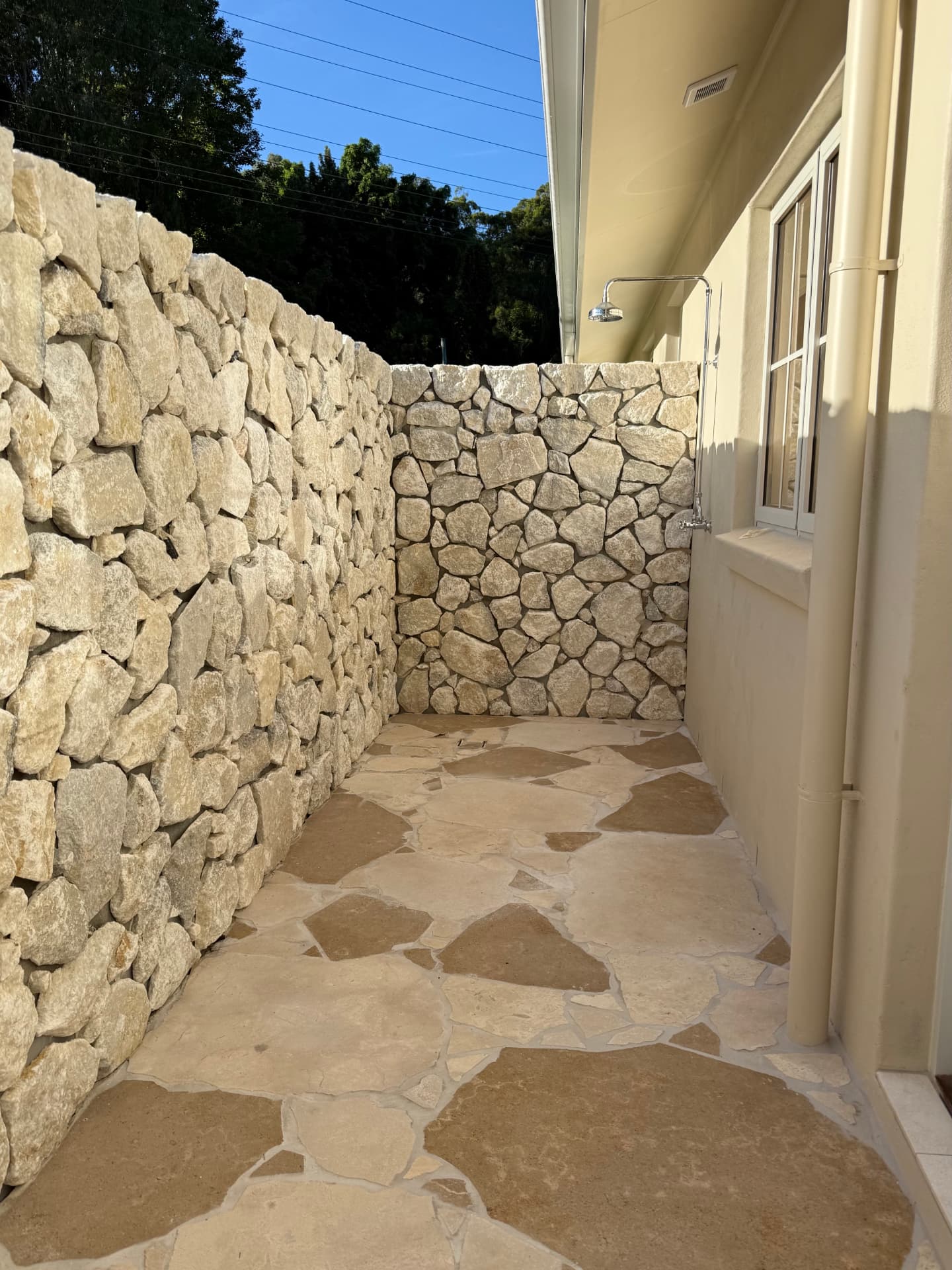 Outdoor shower set into a white crazy paving wall and floor