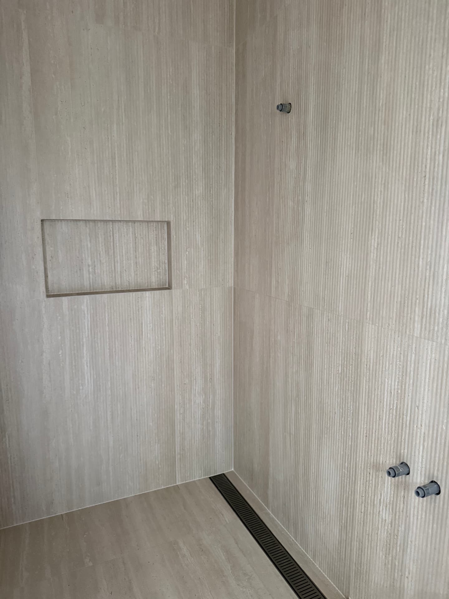 Travertine-look shower walls with a recessed niche and a linear floor drain