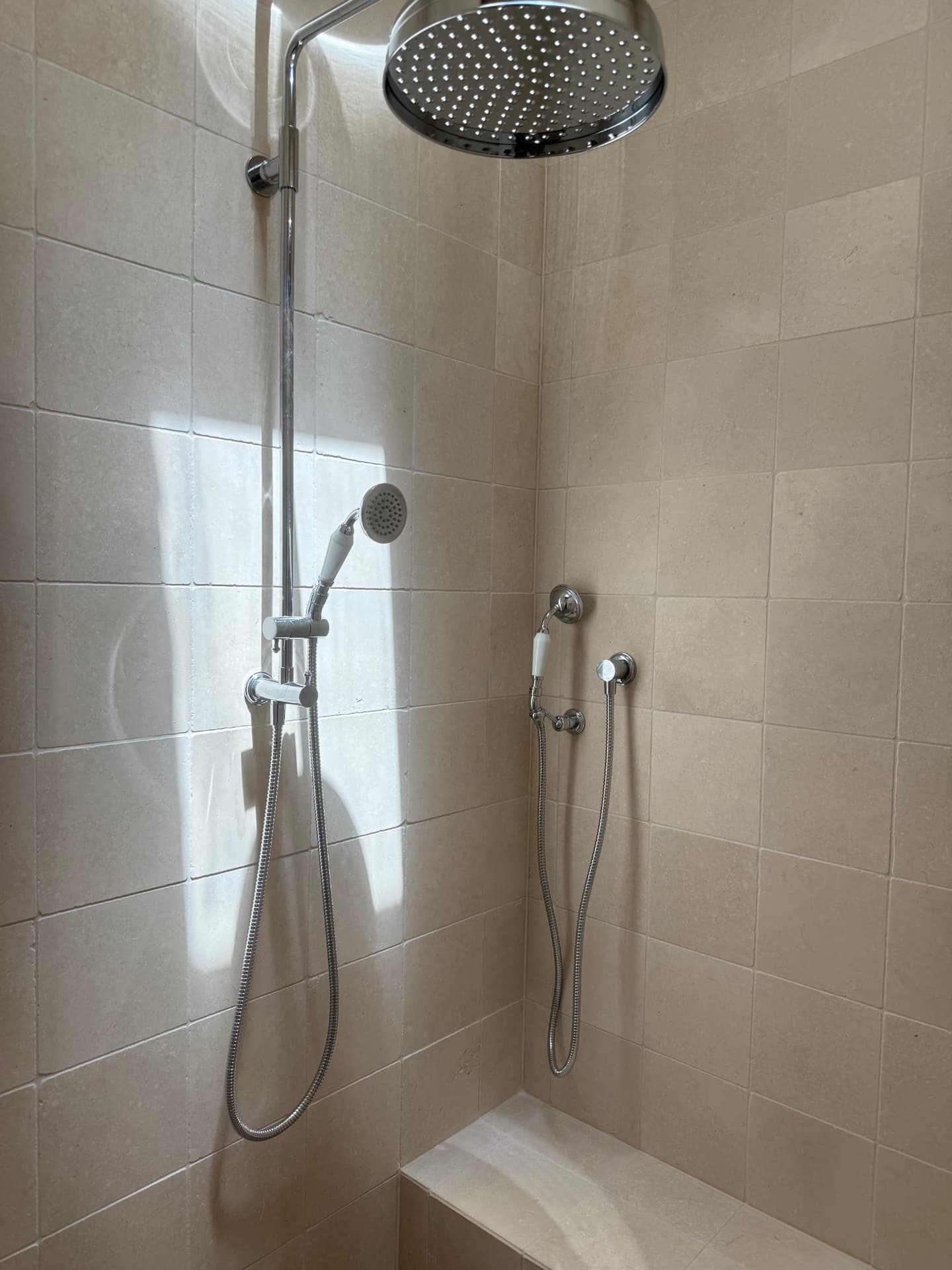 Sunlit tiled shower with overhead and handheld showers, a recessed niche and a bench