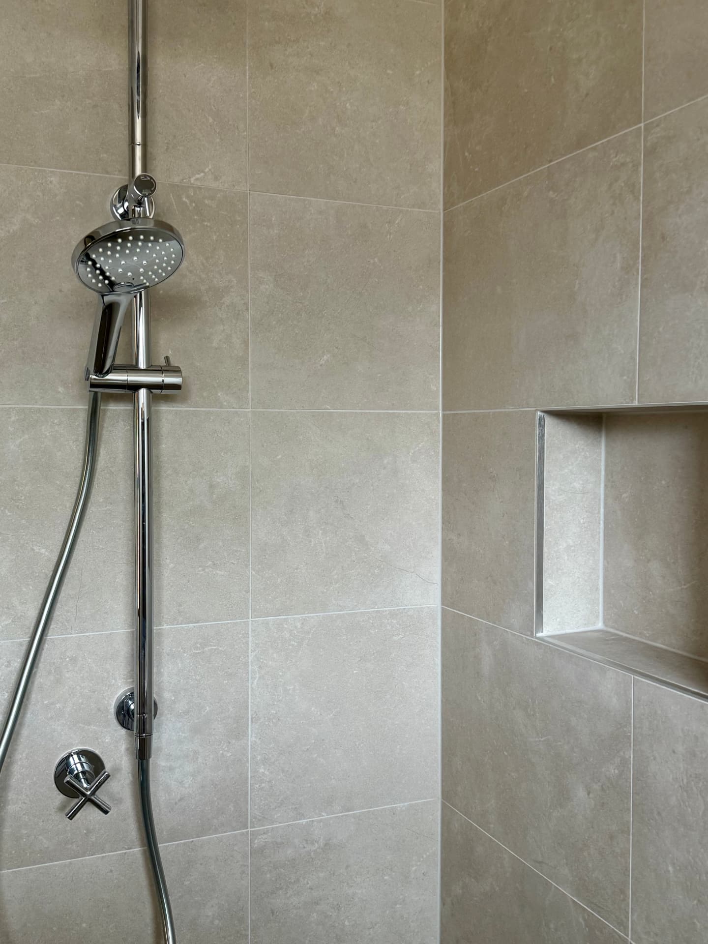 Neutral stone-look shower with a chrome hand shower and recessed niche